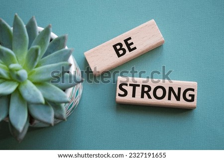 Be strong symbol. Wooden blocks with words Be strong. Beautiful grey green background with succulent plant. Business and Be strong concept. Copy space.