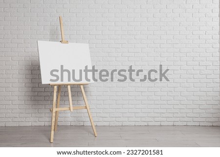 Wooden easel with blank canvas near white brick wall indoors. Space for text Royalty-Free Stock Photo #2327201581