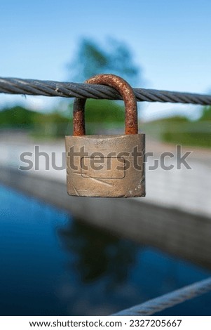 Close-up shot of an old padlock hung from the bridge wires. Symbols of luck and love, unrequited love. There is a text field. Close-up shot of a padlock.