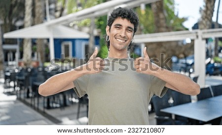 Young hispanic man smiling confident doing ok sign with thumbs up at coffee shop terrace