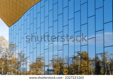 Reflections of trees and blue sky with clouds in the perfect mirror facade of a modern building