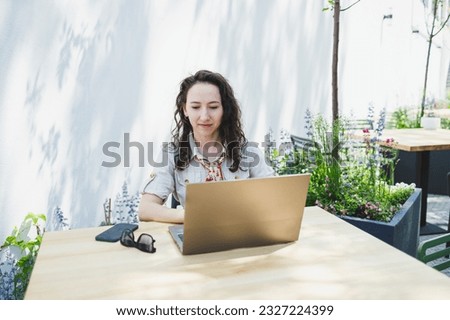 Concentrated female student writing on laptop while studying with cup in cafe, thoughtful freelancer jotting down information for project planning, doing remote work via laptop