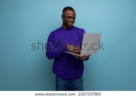 charming young african guy in a blue sweatshirt works remotely on a laptop