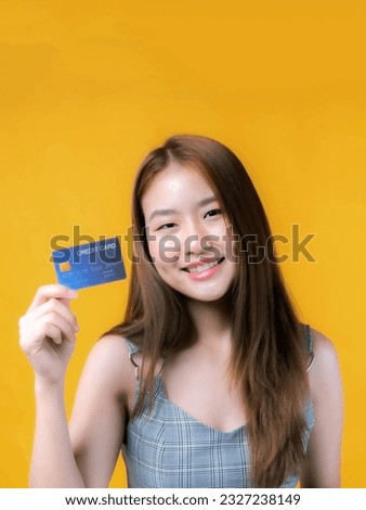 Asian girl showing credit card for payment shopping online and - paying by credit card isolated on yellow - online shopping  e-commerce telemarketing concept 