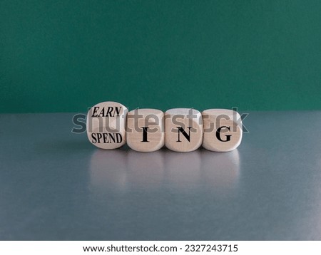 Earning or spending symbol. Turned cubes and changes the word spending to earning. Beautiful green background, grey table. Copy space. Business and earning or spending concept.
