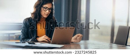 Asian business woman sitting at a table in an office, typing on her laptop with focus. Young female professional showing a dedication and commitment to her project at work. Royalty-Free Stock Photo #2327245825