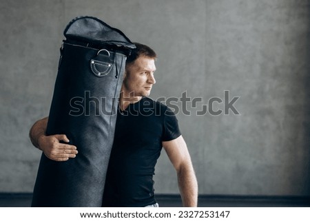 Portrait of guy in black t-shirt holding punching bag