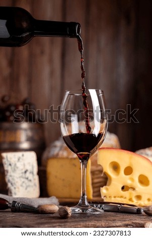 glass of red wine with bottle serving the glass on table with board of various cheeses country bread nuts with wooden background