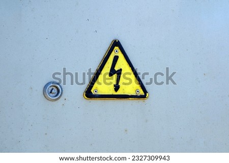 Electrical hazard sign with black lightning in a yellow triangle on a gray painted metal junction box