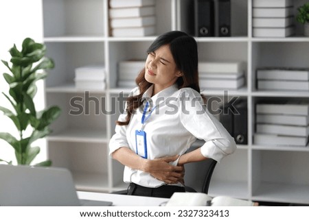 Asian woman working hard in the office having aches and pains in her torso and waist Royalty-Free Stock Photo #2327323413