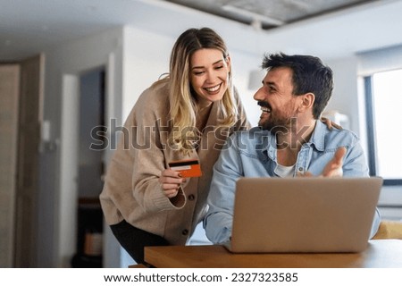 Cheerful young couple using laptop and smiling while shopping online at home Royalty-Free Stock Photo #2327323585