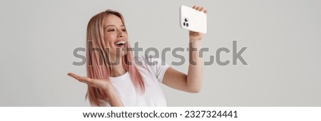 Happy young woman in casual wear jumping taking selfie holding mobile phone over gray background, full length