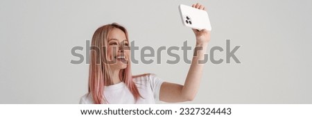 Happy young woman in casual wear standing taking selfie holding mobile phone over gray background, full length