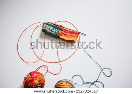 knitting with knitting needles by the magic loop method from multi-colored yarn on a white background