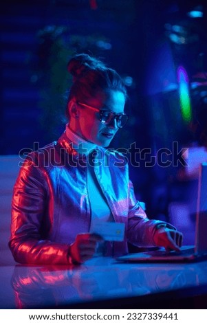 Neon metaverse futuristic concept. modern woman in glasses with laptop and credit card in modern office.