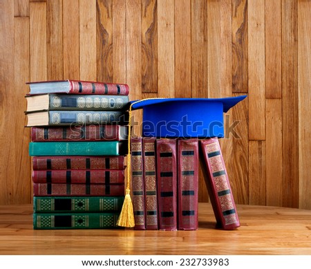Graduation mortarboard on top of stack of books on wooden background of wall