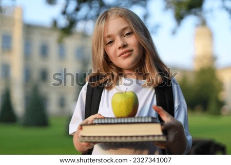 Portrait of a schoolgirl holding a book and an apple in her hands on the background of the school.