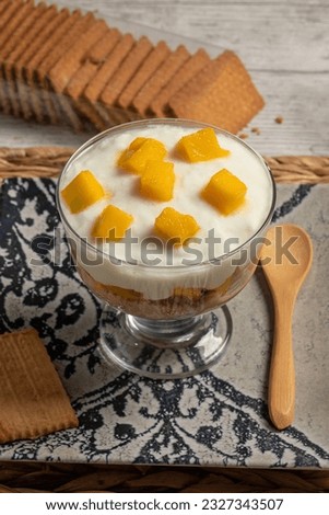 Delicious glass of cold yogurt mousse with mango and biscuit, dark food style. Vertical photo for recipe or menu and selective focus