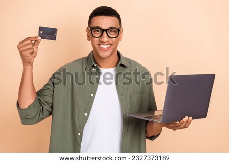 Photo of toothy beaming intelligent guy dressed khaki shirt holding laptop demonstrate credit card isolated on pastel color background