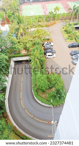 the view that is seen from above presents beauty with the road that goes down to the alley and neatly parked cars and a basketball court when you see it you want to immediately play basketball