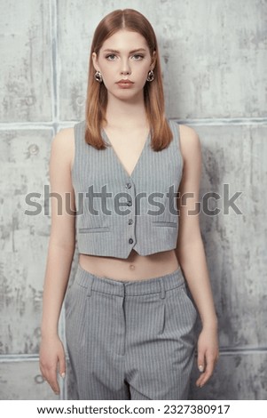 Portrait of a beautiful blonde girl in grey stylish costume of vest and trousers on a grey studio background. Summer fashion. Youth style. Royalty-Free Stock Photo #2327380917