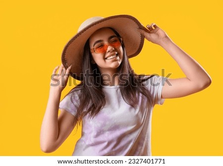 Beautiful young woman wearing stylish sunglasses and hat on yellow background