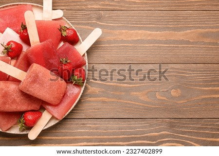 Plate with sweet strawberry ice-cream popsicles on wooden background