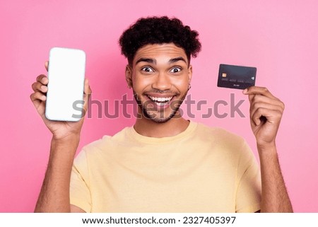 Photo of impressed excited ecstatic crazy guy wear yellow t-shirt hold debit show screen of smartphone isolated on pink color background