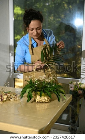 Female florist arranging a flower bouquet, inserting palm leaves into soaked foam in a wicker basket in floral shop. Small business. Creative people. Hobby. Arrangements and gifts for festive events