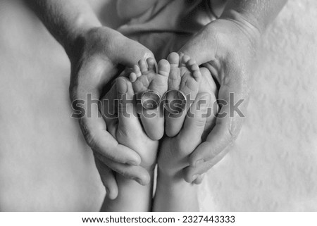 Children's foot in the hands of parents.Mom and dad are holding the baby's legs. Feet of a small newborn baby with his parents' wedding rings. Happy family concept. Black and white photo. Royalty-Free Stock Photo #2327443333