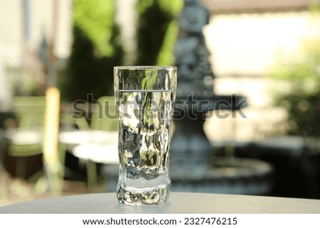 Glass of fresh water on light grey table outdoors