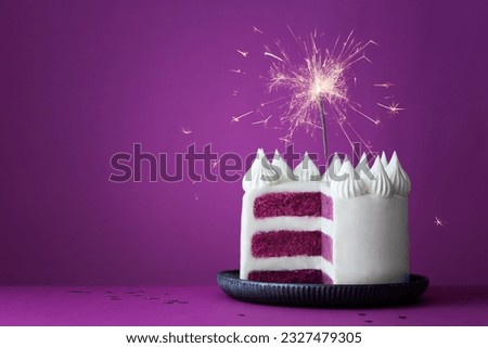 Purple birthday celebration layer cake with white frosting and celebration sparkler against a purple background