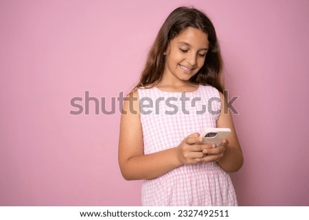 Cute preschooler little girl stand isolated on pink studio background using modern smartphone, smart small kid browsing surfing internet watch cartoon on cellphone, easy access, blank copy space