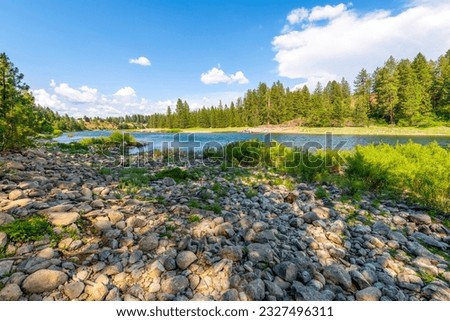 The rocky riverbank and shoreline of the Spokane River as it runs through the small town of Post Falls, Idaho, at McGuire Park. Royalty-Free Stock Photo #2327496311