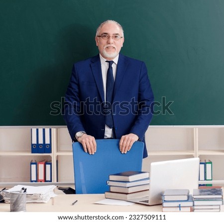 Aged male teacher in front of chalkboard