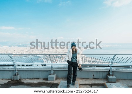 Woman tourist Visiting in Hakodate, Traveler in Sweater sightseeing view from Hakodate mountain with Snow in winter. landmark and popular for attractions in Hokkaido, Japan.Travel and Vacation concept