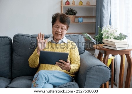 Smiling Asian seniors embrace a fulfilling retirement lifestyle at home, connecting with family through vibrant online video conference calls on their taplet. Radiating happiness and cherishing