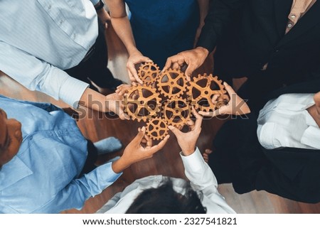 Office worker holding cog wheel as unity and teamwork in corporate workplace concept. Diverse colleague business people showing symbol of visionary system and mechanism for business success. Concord Royalty-Free Stock Photo #2327541821