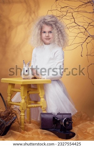 Blond adorable minor girl with white rabbit. Fairy postcard. Alice in Wonderland.
