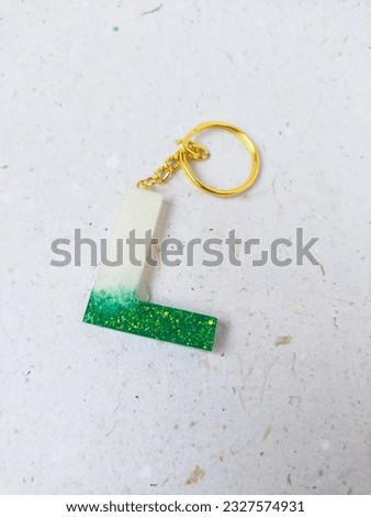 Green and white glitter epoxy resin L alphabet keychains on a white background. Resin alphabet pattern gold keychain. Royalty-Free Stock Photo #2327574931