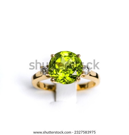A vibrant peridot gemstone graces the center of a glossy, tarnish-resistant, yellow gold ring. The ring is accented with multiple pave-set  diamonds, sparkling exquisitely to complement the main stone