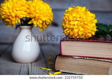 Flowers. Beautiful yellow chrysanthemum in a vintage vase. Old books on a wooden background.