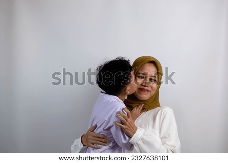 A 4 year old Asian boy kisses his mother's cheek passionately and affectionately on a white background isolated