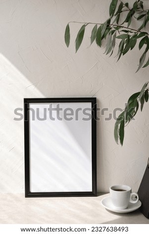Minimalist elegant neutral empty picture frame mockup with geometric sunlight shadow, coffe cup, template for art work poster with copy space. Neutral modern home interior, workspace, beige background