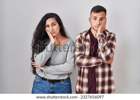 Young hispanic couple standing over white background thinking looking tired and bored with depression problems with crossed arms. 