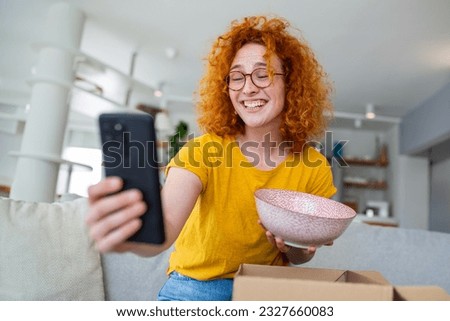 A red-haired woman gleefully photographs the pot she ordered online, capturing the excitement of its arrival. Her radiant smile showcases the joy of culinary discovery in this captivating stock image.