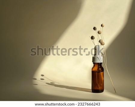Glass bottle with serum and dried flower branch on a beige background with sunlight on it. Skincare