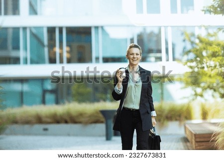 happy modern woman worker in business district in black jacket with cup of coffee walking. Royalty-Free Stock Photo #2327673831