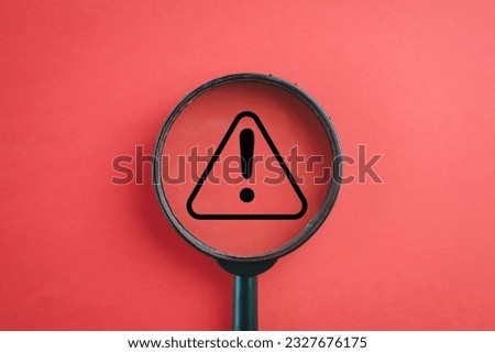 View through a magnifying glass on Exclamation mark or Warning sign over red background Attention sign,Exclamation mark,warning sign concept. Royalty-Free Stock Photo #2327676175