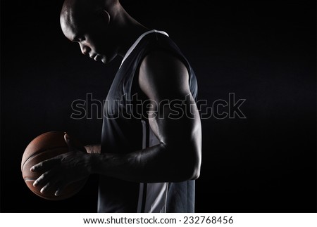 Side view of fit young basketball player holding ball against black background with copy space. African american basketball player with ball.